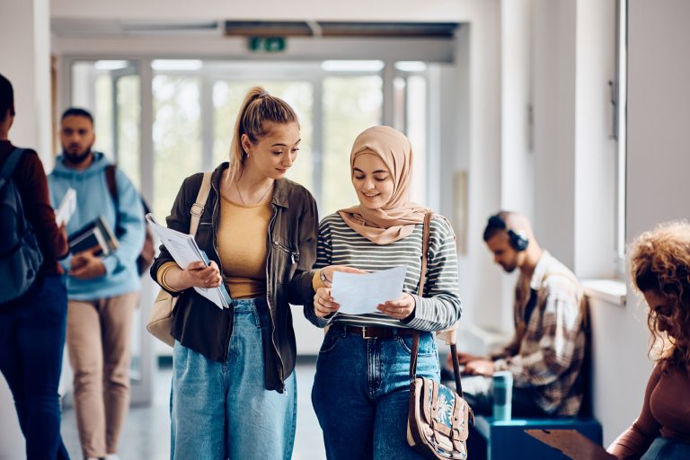 Happy student and her friend reading their exam results while walking through university hallway.