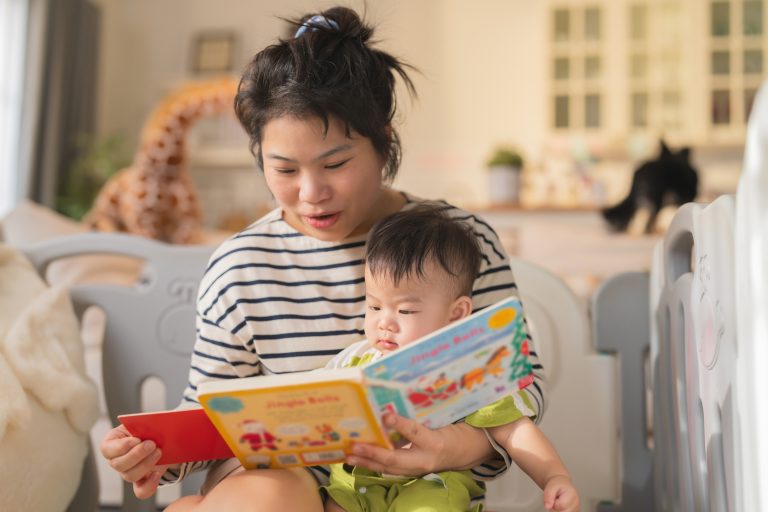 Young mother reading bedtime storybook to baby Asian baby boy sitting