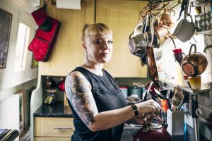 White woman in her 30s making a cup of tea on her houseboat